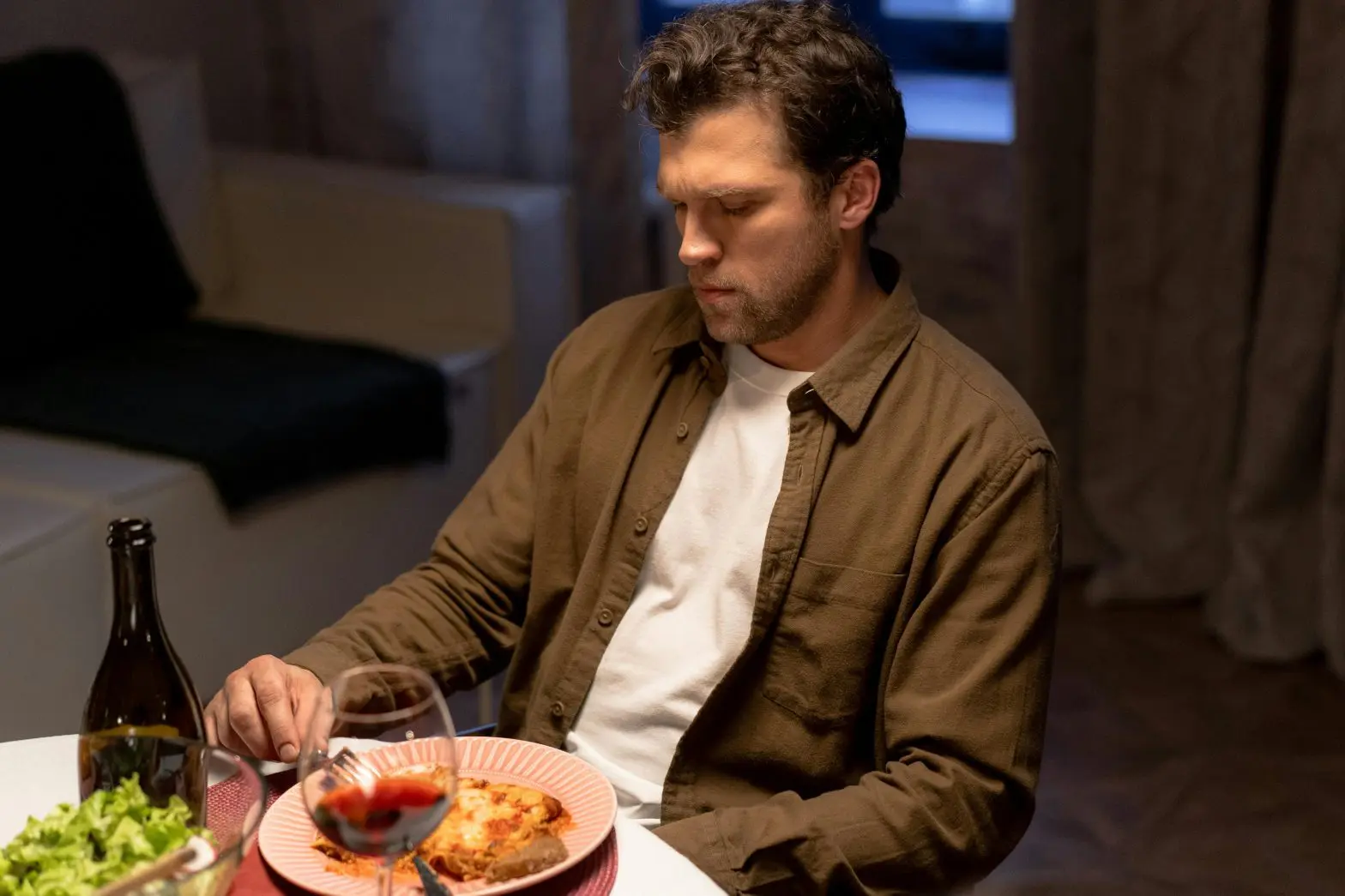 A man sitting at a table staring at his food because of alcoholism and not eating.